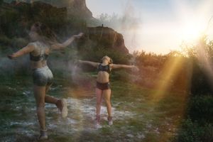 Two dancers move through powder in warm golden sunlight with lens flare over a desert landscape of grass and rocky cliffs.