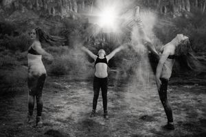 Black and white triple exposure of a dancer posing with powder and a bright sunburst over a rugged desert landscape.