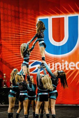 A cheerleader balances in an extended stunt held by teammates in teal and black uniforms at a United Spirit Association competition.