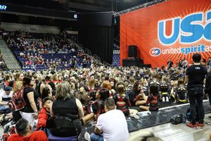 Large crowd of cheerleaders and spectators fills an arena at a USA United Spirit cheerleading competition beneath an orange banner.