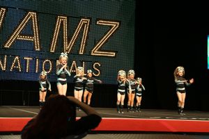 Youth cheerleading team in black and teal uniforms performs a routine on stage at the JAMZ Nationals competition.