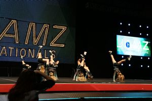 Cheerleaders in black uniforms perform back-bend and handstand stunts on stage in front of the JAMZ Nationals lighted sign.