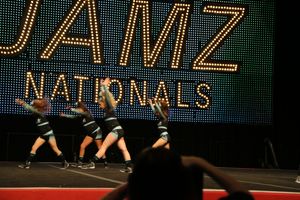 Cheerleading team in black and silver uniforms performs a dance sequence on stage at the JAMZ Nationals cheer competition.