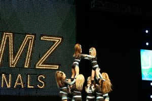 Cheerleading team builds a tall pyramid stunt on stage with a flyer lifted high at the JAMZ Nationals competition.