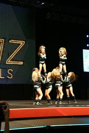 Two young flyers balance atop a cheerleading pyramid while teammates support them on the JAMZ Nationals stage.