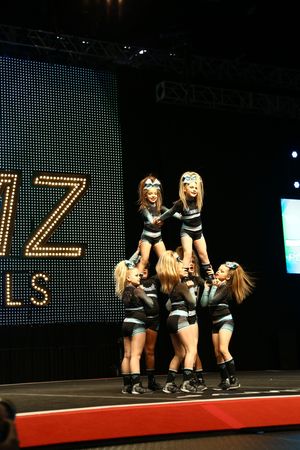 Cheer team performs a pyramid stunt with two flyers held high while teammates support below on a competition stage.
