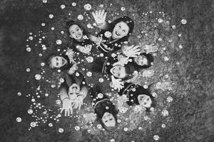 Black and white overhead photo of smiling cheerleaders lying in a circle with raised hands among scattered glitter and confetti.