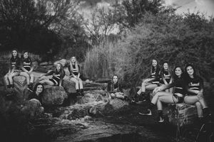 Black and white photo of a group of girls in matching athletic wear posing on rocks beside trees in a natural outdoor setting.