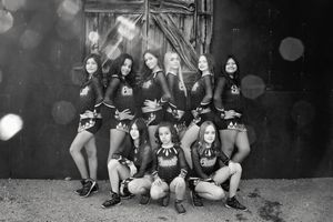 Black and white group portrait of cheerleaders in matching uniforms posing in front of an old barn door with soft light flares.