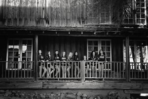 Black and white photo of a cheer team in matching uniforms standing along the railing of a rustic wooden porch.