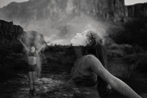 Black and white double exposure of a woman with her head tilted back and a dancer tossing powder against a rocky landscape.