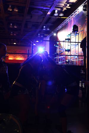 Silhouetted cheerleaders huddle together backstage under bright blue stage lights before a competition performance.