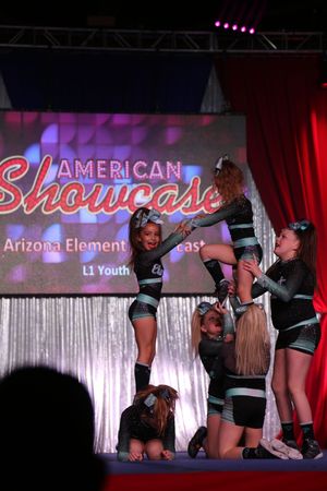 Youth cheerleaders perform a stunt at the American Showcase competition, lifting a teammate beside a stage screen reading Arizona Element.
