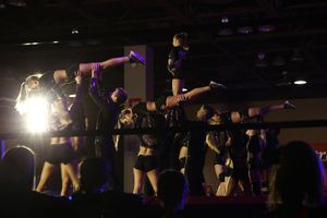 A cheer team performs an extended stunt with flyers balanced overhead as spectators watch from the foreground.