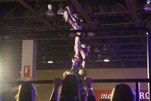 A cheerleader is lifted upside down in a dramatic stunt while an audience watches at an indoor cheer competition.