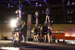 Cheerleaders hold flyers high in a synchronized stunt formation under bright lights at a cheer competition.