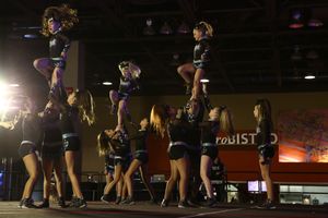 Cheer team performs a stunt sequence with flyers lifted high on a competition floor in a large arena.