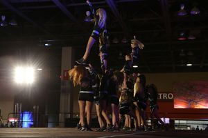 Cheerleaders hoist a flyer into the air in a pyramid formation during a competition routine.