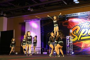 A flyer balances atop her teammates in a cheer stunt as other squad members perform nearby on the competition floor.