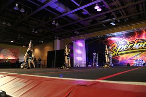 Cheerleaders perform a routine on the mat while one athlete does a handstand at a Spectacular cheerleading competition.