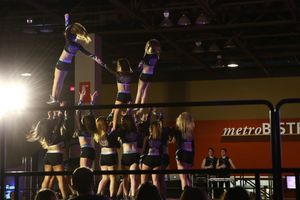 Cheerleaders in black uniforms perform a stunt on stage at a competition, with a flyer lifted high above the team.
