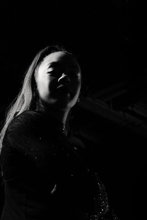 Black and white low-key portrait of a smiling woman in a sparkly top with long hair, lit from the side against a dark background.