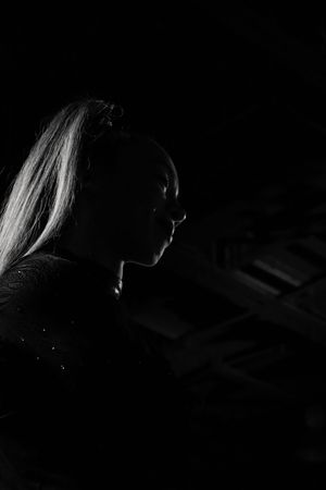 Black and white silhouette of an athlete in profile with a high ponytail, rim-lit against a dark background with ceiling beams above.