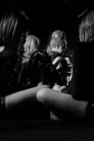 Black and white photo of cheerleaders with styled hair sitting close together in a dim venue before a competition performance.