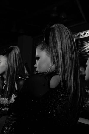 Dramatic black and white side profile of a cheerleader with a high ponytail and glittering uniform in a dark arena.