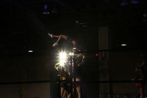 A cheerleader is lifted high in the air as a bright stage light glows behind teammates during a dark arena performance.