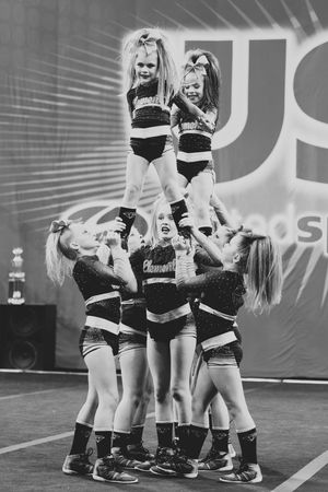 Black and white photo of a youth cheer team building a pyramid stunt with two small flyers lifted high above their teammates.