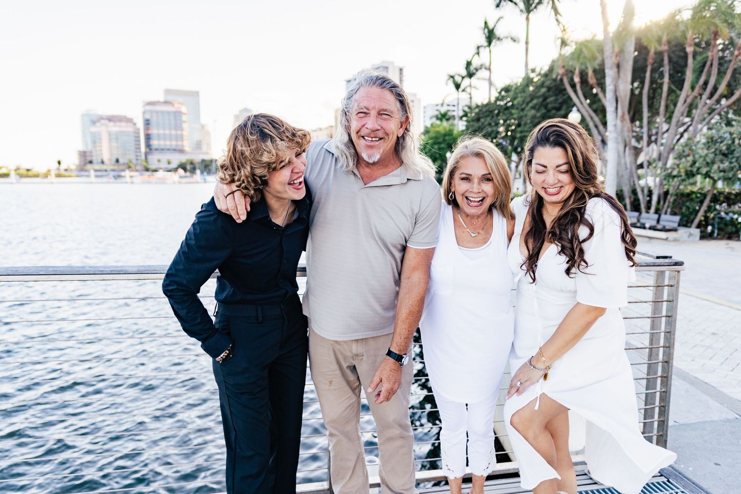 Four people laughing together outdoors near a waterfront on a sunny day, dressed in casual and elegant attire downtown west palm beach.