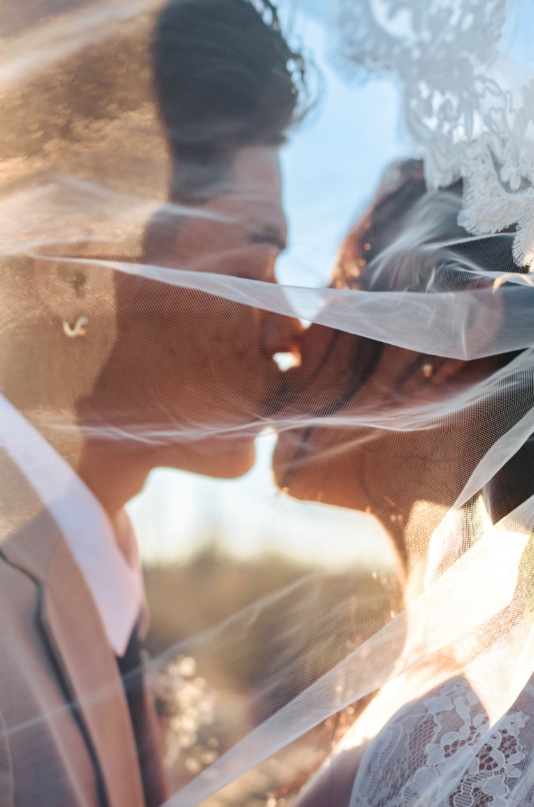 Bride and groom kiss behind a veil.