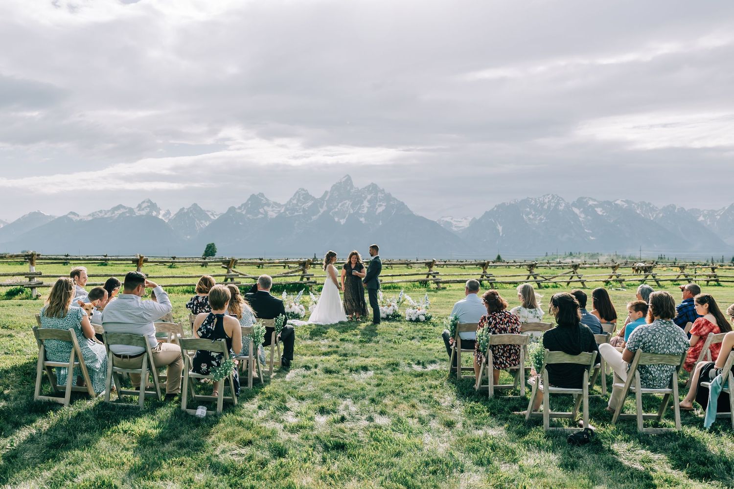 Intimate outdoor wedding ceremony with guests seated in a grassy meadow overlooking the Grand Teton mountain range in Wyoming.