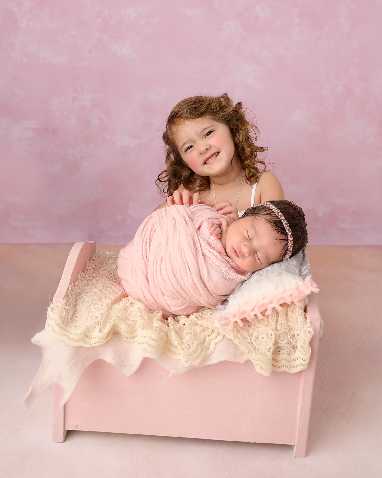 Older sister gently posing beside her newborn baby sister during a sibling newborn photography session in Zephyrhills, Florida.