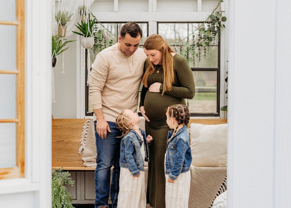 Parents sharing a candid moment with their two young daughters during a greenhouse family photography session in Millville, NJ