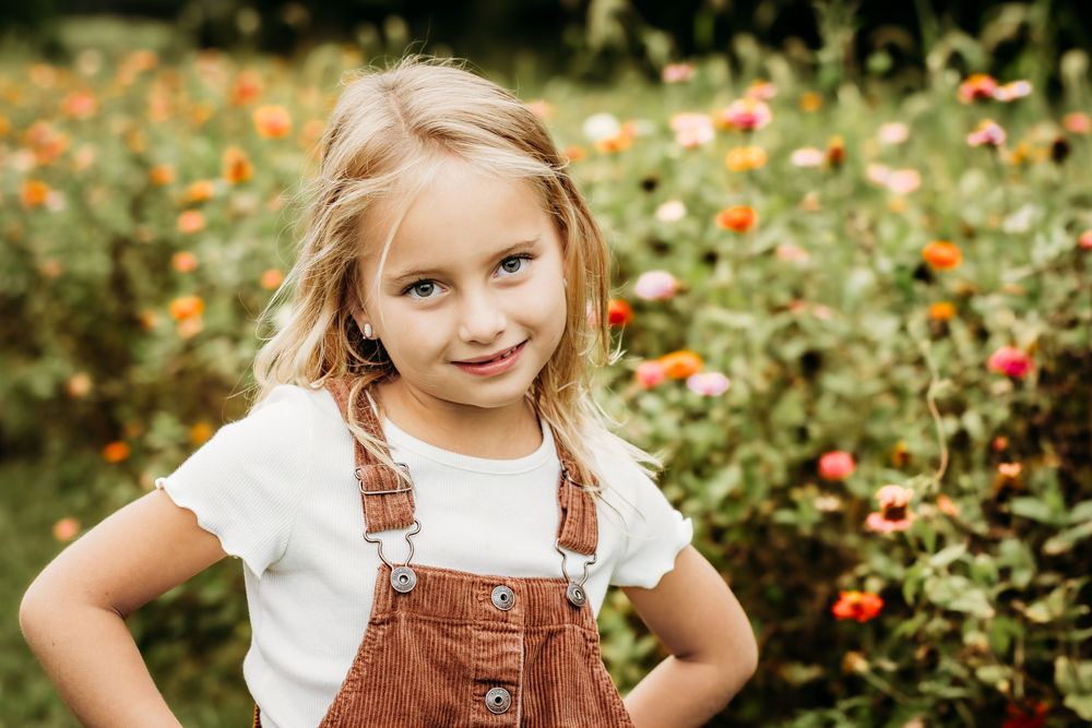 Young girl smiling among colorful flowers during an outdoor family portrait session in Mullica Hill, NJ.