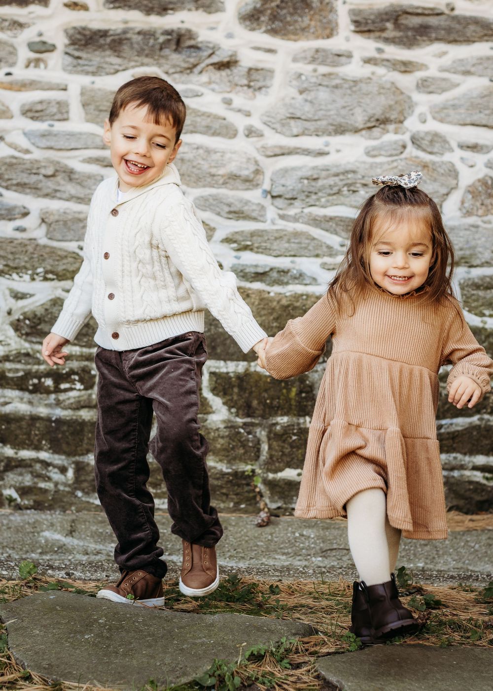 Young brother and sister holding hands and laughing during a family photography session.