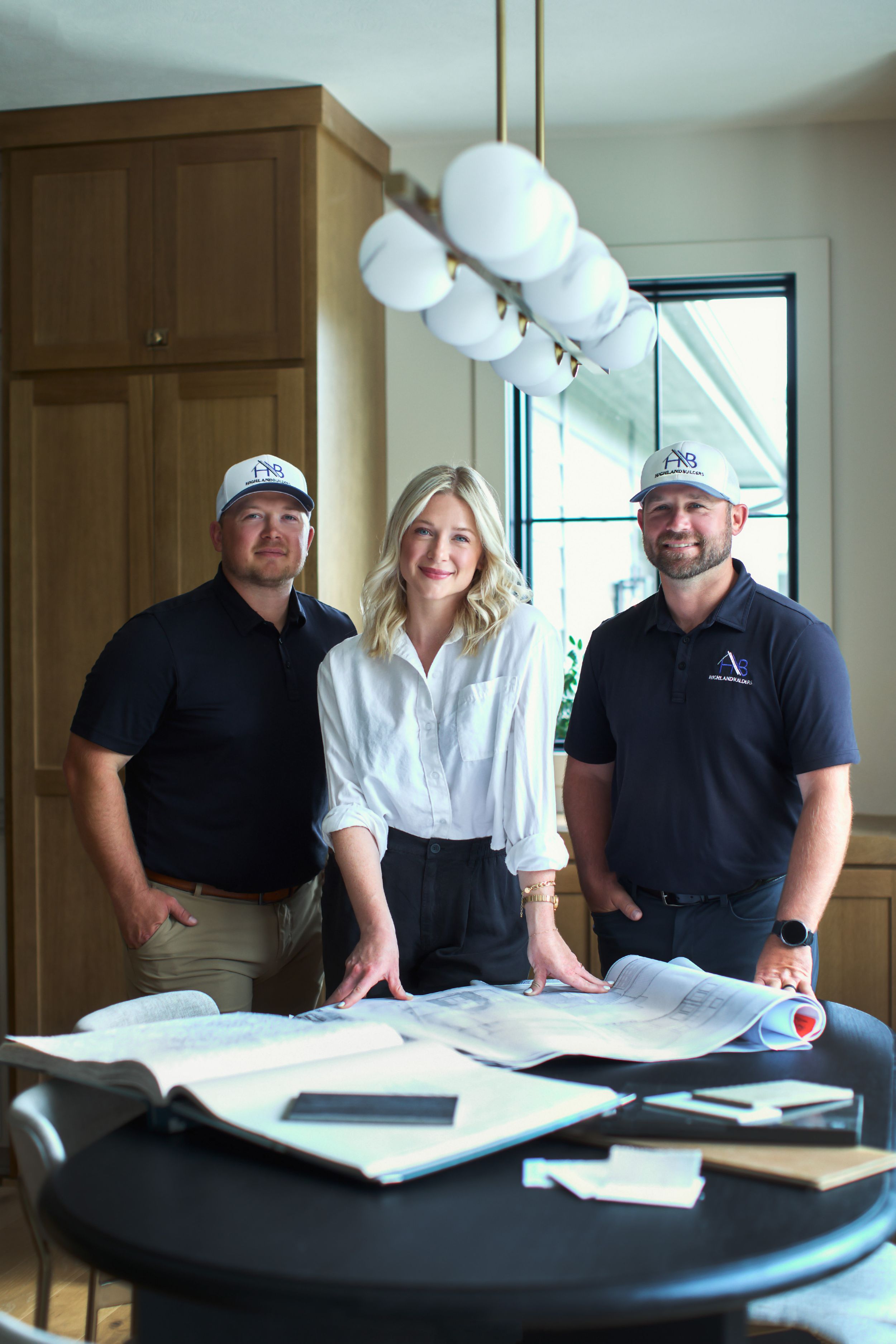 Three professionals reviewing architectural blueprints at a table in a modern interior design studio.