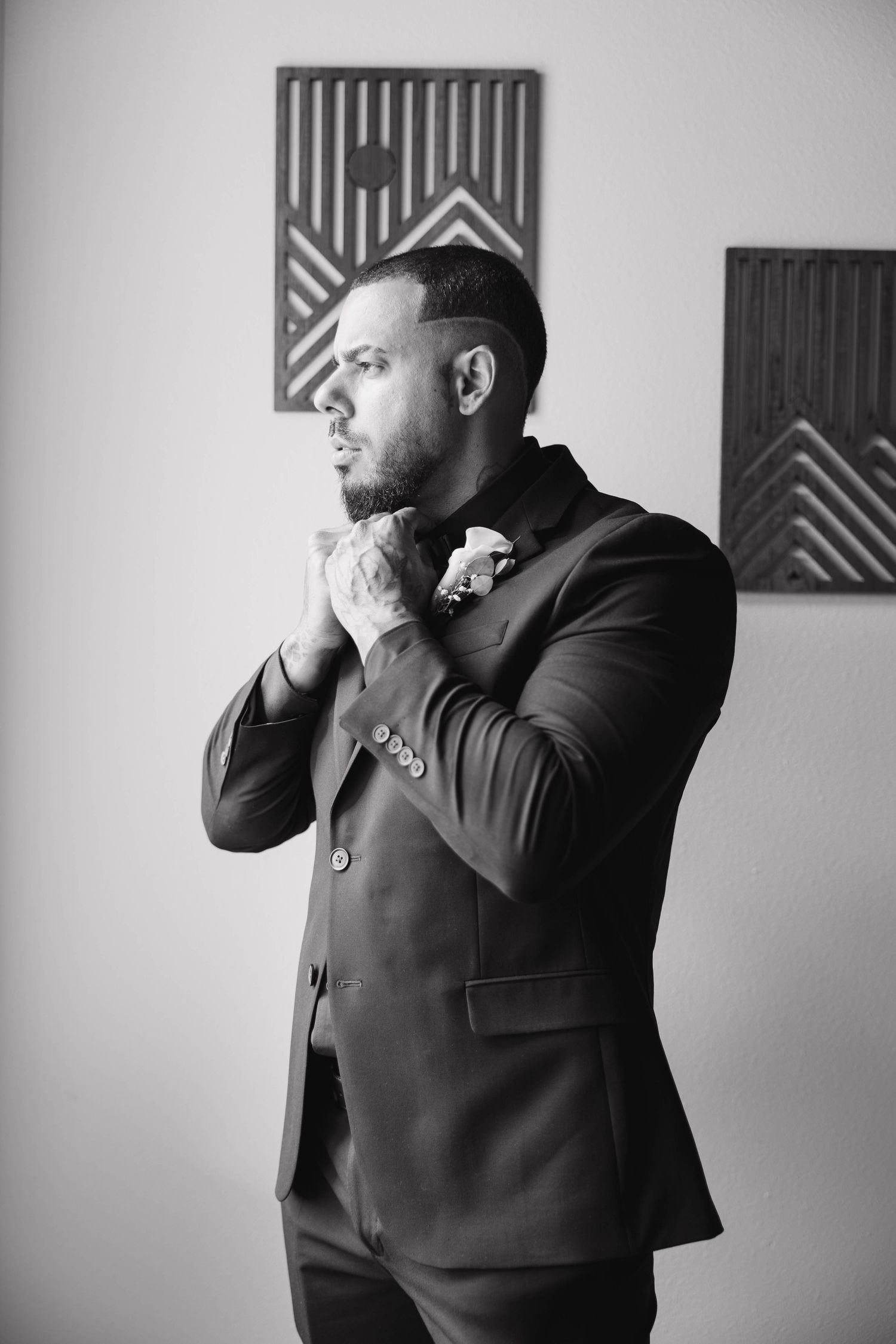 Black and white photo of a groom in a suit adjusting his tie before wedding ceremony.