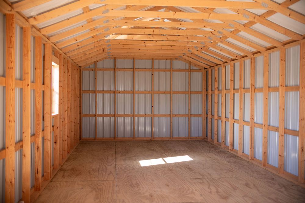 Interior view of an empty wooden shed with metal walls, exposed rafters, and a plywood floor bathed in natural light.