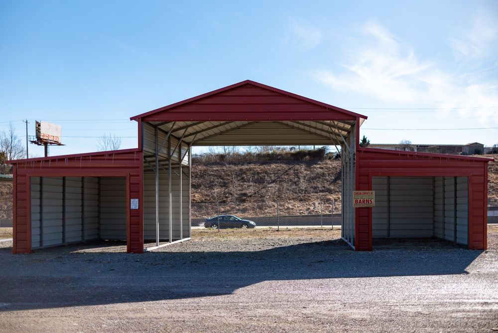 Red metal carport with triple bays and peaked roof on gravel lot with open countryside background.