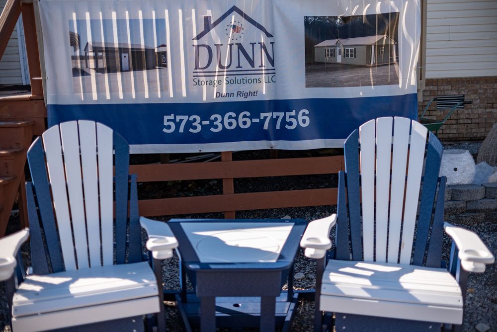 Two blue and white Adirondack chairs displayed in front of a Dunn Construction Solutions LLC banner with phone number 573-366-7756.