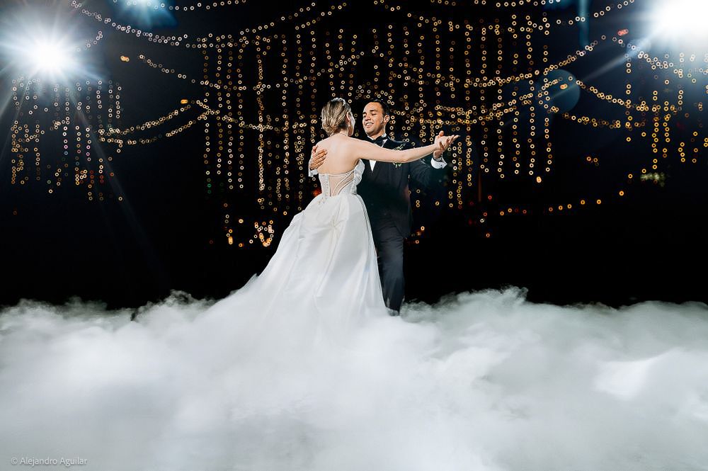 Bride and groom share first dance on fog-covered floor under sparkling string lights at elegant wedding reception.