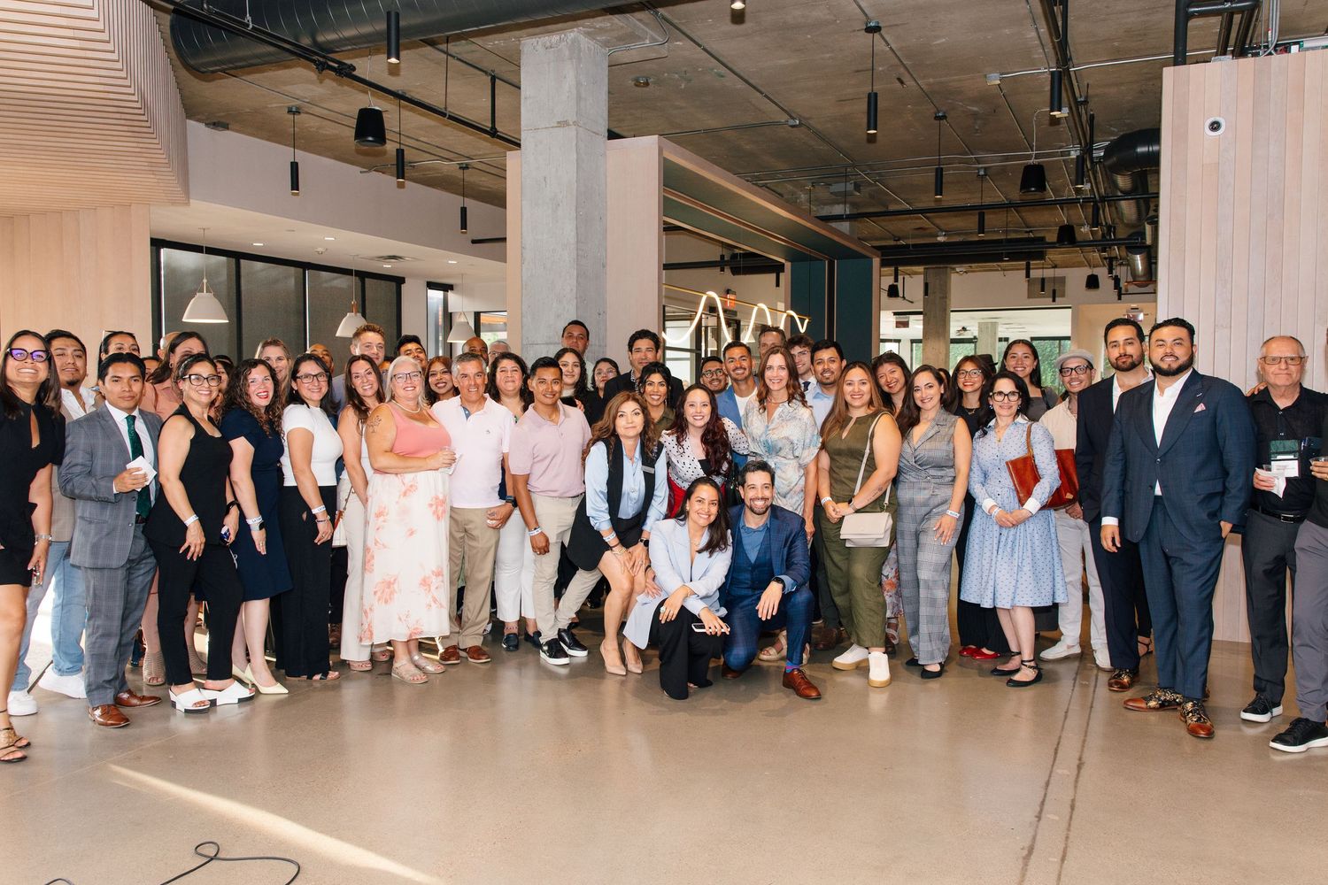 Large diverse group of professionals posing together in a modern open office space during a corporate event.