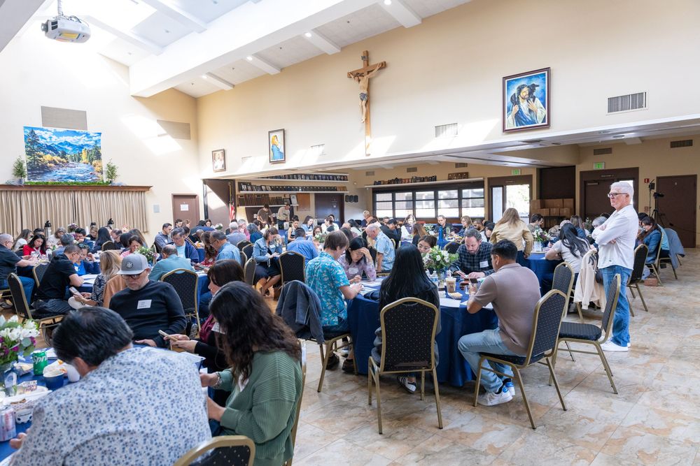 Large group of people dining together in a Catholic church hall with a crucifix on the wall.