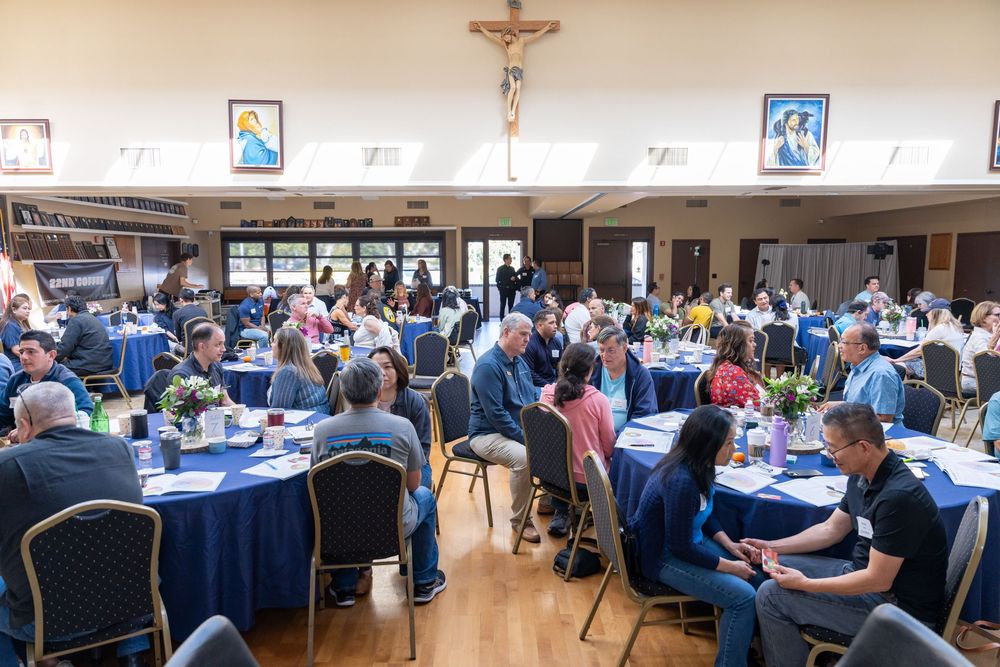 Large church hall banquet with guests seated at round tables adorned with blue linens and floral centerpieces.