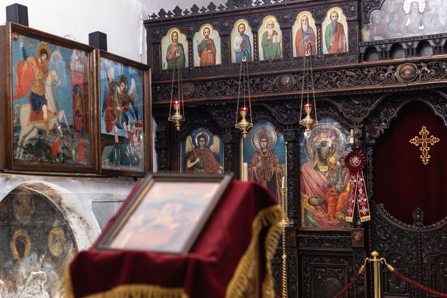 Orthodox church interior with ornate wooden iconostasis and colorful religious icons displayed on walls and altar screen.