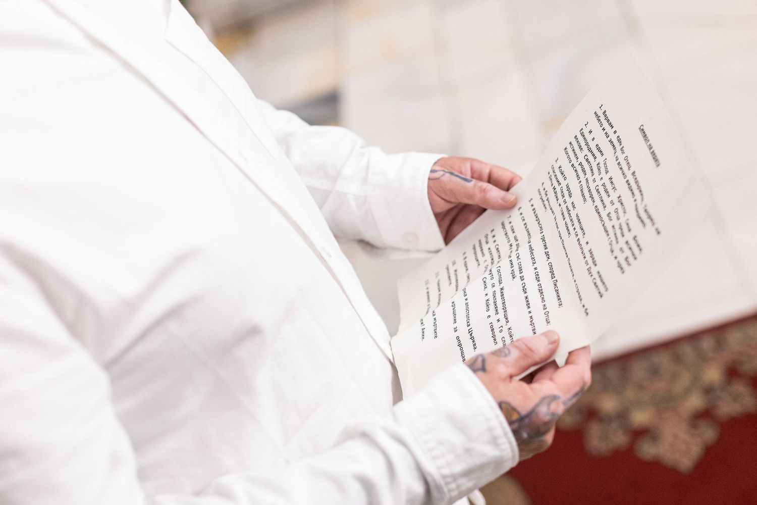 Person in white attire holding a printed document or speech paper outdoors at a formal event.