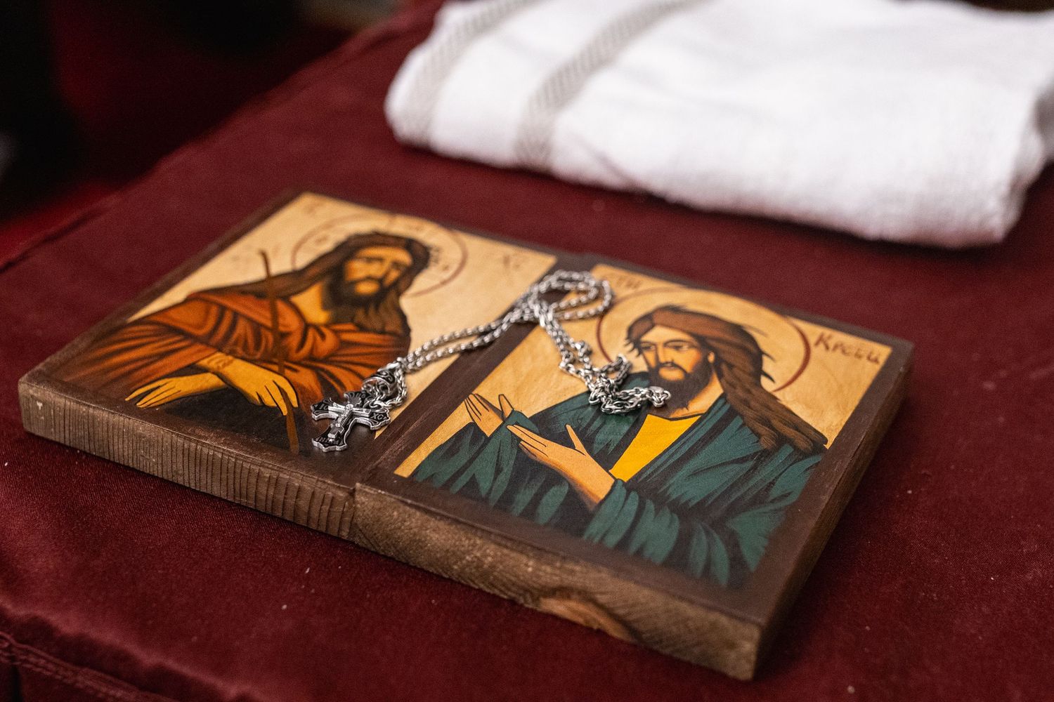 Two religious icons depicting saints on a wooden diptych with a silver chain necklace on red velvet.